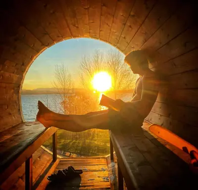 a man sitting on a bench reading a book with the sunset at Estello Suites & Spa in Lac-Mégantic