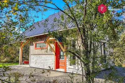 a house with a red door and a tree at L'Ermite - Rustique Écoresponsable Dans la nature in Notre-Dame-Des-Bois
