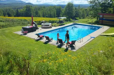 two people are walking by a swimming pool at Spacious luxurious Villa, bright cottage, pool, Jacuzzi, sauna, nature in Mansonville