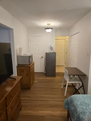 a room with a bed and a table and a refrigerator at Doux cocon in Saint-Jean-sur-Richelieu