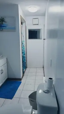 a white bathroom with a toilet and a blue rug at CosyRoom in Brossard