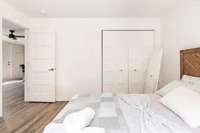 a white bedroom with a large bed with a wooden headboard at Logement neuf, spacieux in Longueuil