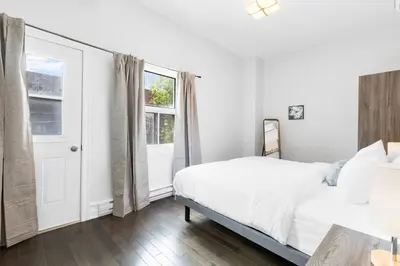 a white bedroom with a bed and a window at The Parc Mile End ApartHotel in Montréal