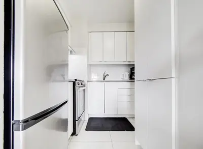a white kitchen with white cabinets and a refrigerator at Cozy 2-Bedroom à Plateau-Mont-Royal in Montréal