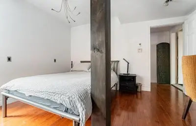 a white bedroom with a bed and a wooden floor at Le Loft in North Hatley