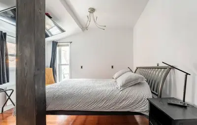 a bedroom with a bed with white walls and wooden floors at Le Loft in North Hatley