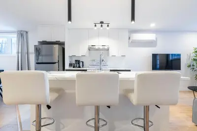 a kitchen with white cabinets and white bar stools at T3 10 mins to La Ronde nice , Cozy 3 bedroom longueuil in Longueuil