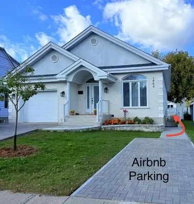 a white house with a sign for african parking at Charmant appartement au sous-sol in Longueuil