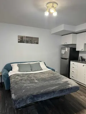 a bedroom with a large bed and a kitchen at Charmant appartement au sous-sol in Longueuil