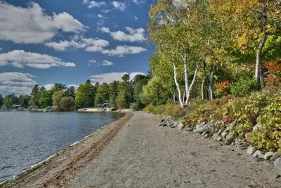 a sandy beach next to a lake with trees at Le Southière, minimum 30 nuits in Magog-Orford
