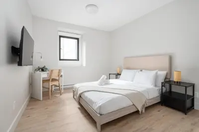 a white bedroom with a large bed and a desk at The Griffin ApartHotel- Downtown in Montréal