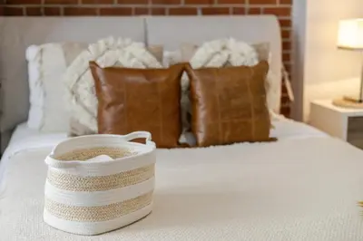 a white bed with pillows and a basket on it at Central 2BDR Condo on Bishop-Vibe Central MTL in Montréal