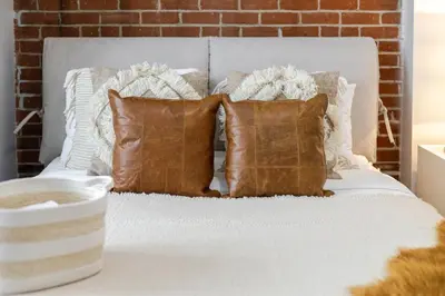 a white bed with brown pillows and a brick wall at Central 2BDR Condo on Bishop-Vibe Central MTL in Montréal