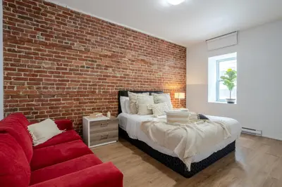 a bedroom with a brick wall and a bed and a red couch at Central 2BDR Condo on Bishop-Vibe Central MTL in Montréal