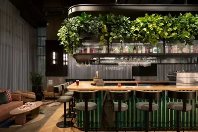 a bar in a restaurant with stools and plants at Moxy Montreal Downtown in Montréal