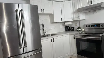 a kitchen with white cabinets and a stainless steel refrigerator at Cozy Terrebonne in Terrebonne