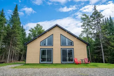 a house with two red chairs in front of it at Chalet Escapade, Spa, Piscine in La Patrie