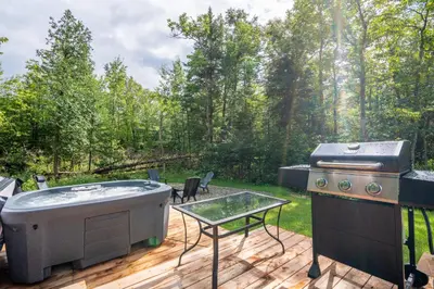 a hot tub and a grill on a deck at Chalet Escapade, Spa, Piscine in La Patrie