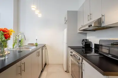 a kitchen with white cabinets and a black counter top at Snug Studio on Bishop DT MTL in Montréal