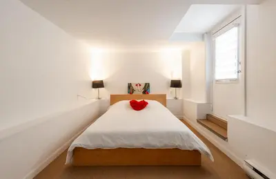a white bedroom with a bed with a red flower on it at Au coeur du plateau!! in Montréal