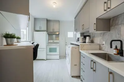 a kitchen with white cabinets and a sink and refrigerator at Grand Urban 4BR Luxe Loft in Griffintown in Montréal