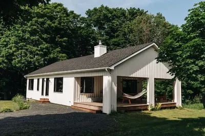 a white building with a porch and a porch swing at Le Fitzsimmons in Mansonville