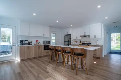 a kitchen with white cabinets and wooden bar stools at Chalet des Oiseaux Bleus, Spa, Lac in Saint-Gérard