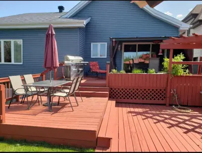 a deck with a table and an umbrella on a house at La campagne en ville avec spa in Laval