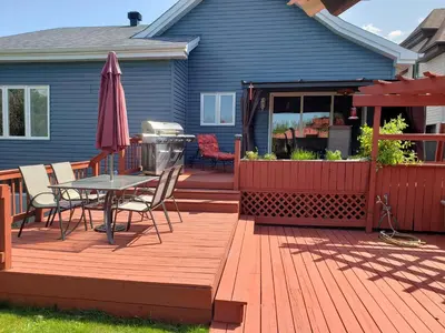 a deck with a table and chairs and an umbrella at La campagne en ville avec spa in Laval
