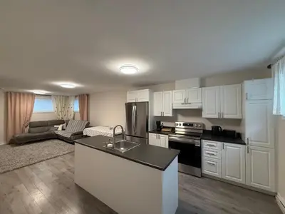 a kitchen with white cabinets and a living room at Confort & Harmonie in Longueuil