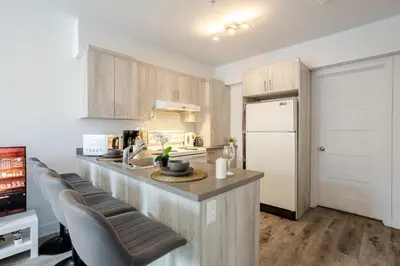 a kitchen with a counter with chairs and a refrigerator at Modern 3BR in Griffintown in Montréal