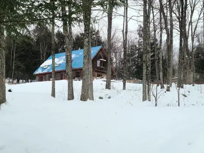 a log cabin with a blue roof in the snow at Détente au coeur de la forêt in Mansonville