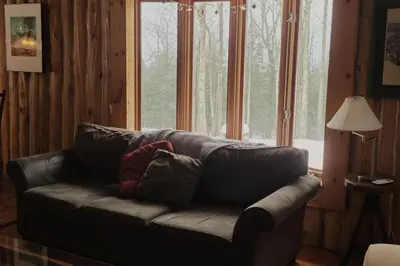 a leather couch in a room with a large window at Détente au coeur de la forêt in Mansonville