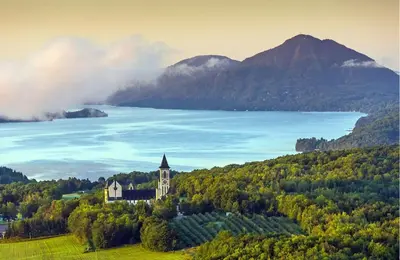 a church on a hill next to a body of water at Détente au coeur de la forêt in Mansonville