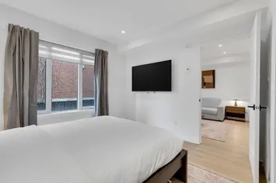a white bedroom with a large bed and a television at Le Victoria Midtown Mtl in Montréal