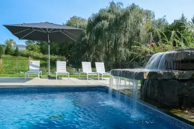 a pool with an umbrella and chairs and a fountain at 891 shefford 4-bedroom house in Bromont