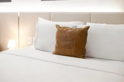 a white bed with a brown pillow on it at Olympia Hotel by Lodgo in Montréal