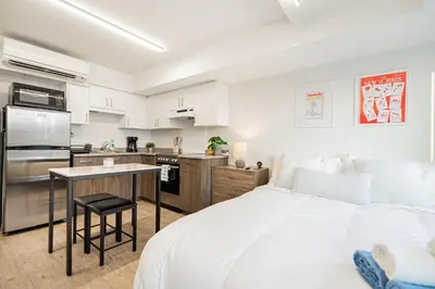a white bedroom with a large bed and a kitchen at Top Location - Cozy & Bright MTL studio near metro in Montréal