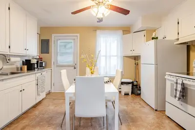 a kitchen with a white table and white appliances at Appartement moderne 3 chambres avec spa, jardin privé & parking gratuit - accès autonome in Saint-Jean-sur-Richelieu