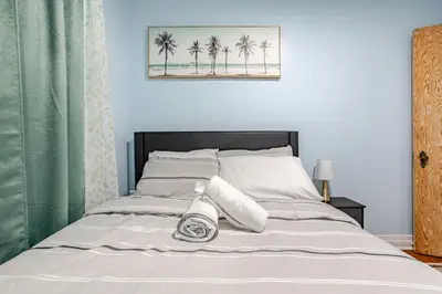 a bedroom with a bed with white sheets and palm trees at Appartement moderne 3 chambres avec spa, jardin privé & parking gratuit - accès autonome in Saint-Jean-sur-Richelieu
