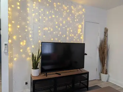 a flat screen tv sitting on a stand next to a wall with lights at Espace Cozy - 2 bed in Longueuil