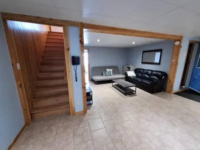 a living room with a leather couch and a stairway at Le Repos Du Lac Aylmer in Disraeli