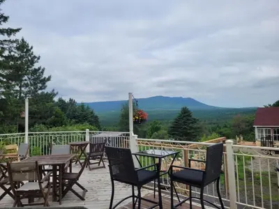 a deck with tables and chairs with mountains in the background at Gîte champêtre Chesham in Notre-Dame-Des-Bois