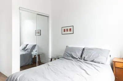 a white bedroom with a bed and a mirror at Appart lumineux et chaleureux in Montréal