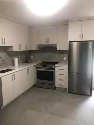 a kitchen with white cabinets and a stainless steel refrigerator at Peaceful oasis near airport private entrance in Pointe-Claire