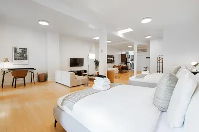 a white bedroom with two beds and a living room at Sunny Open Loft in Montréal