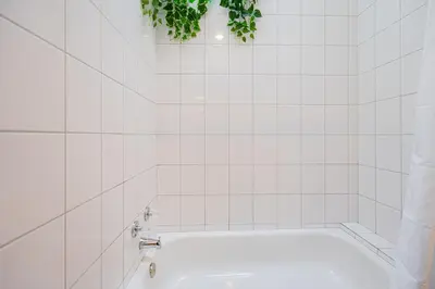 a white tiled bathroom with a tub and a plant at Sunny Open Loft in Montréal