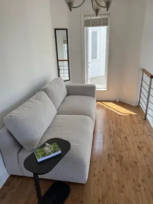 a living room with a gray couch and a table at Chambre queen near Montreal in Sainte-Catherine