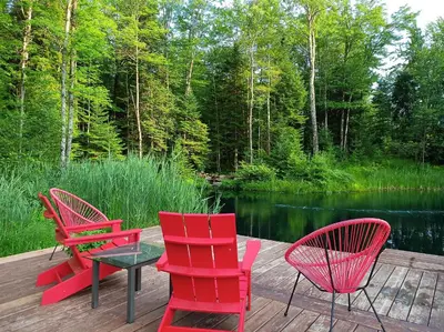 four red chairs and a table on a deck next to a lake at Private Hummingbird Room - Modern & Cozy in Mansonville
