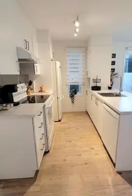 a kitchen with white cabinets and a white refrigerator at MTR Apart Montreal Hospital Corporate Stay in Longueuil